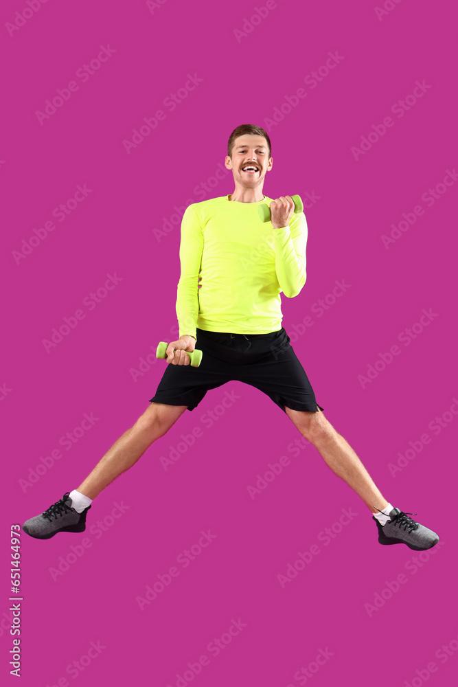 Sporty jumping young man with dumbbells on magenta background