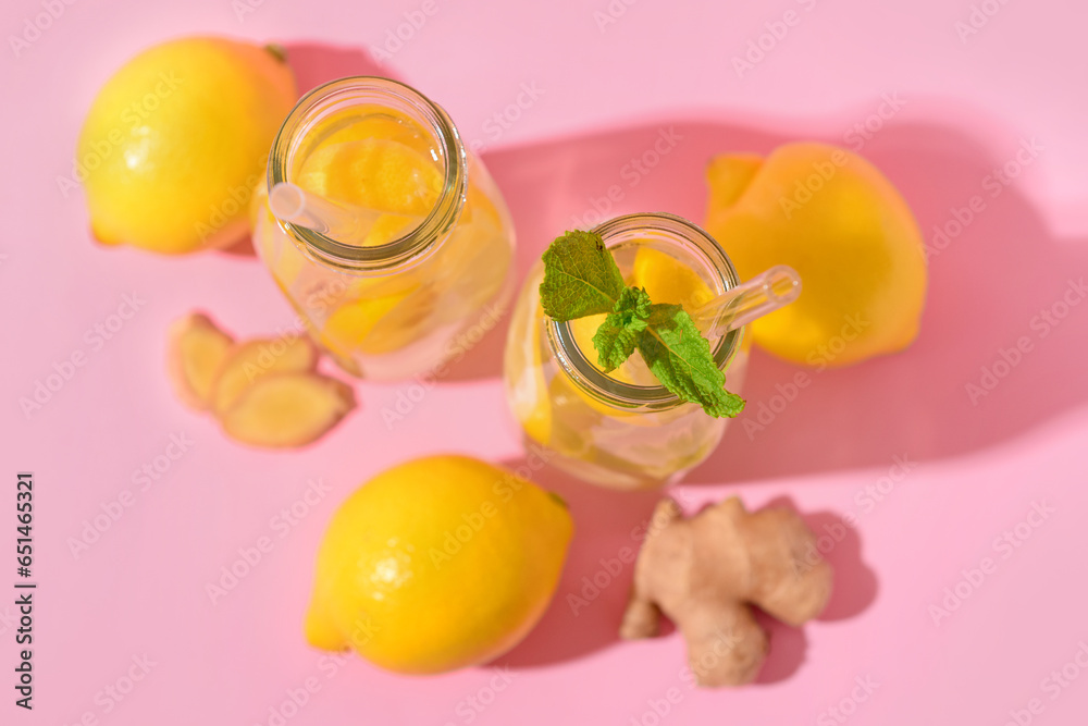 Bottles of tasty lemonade with ginger and mint on pink background