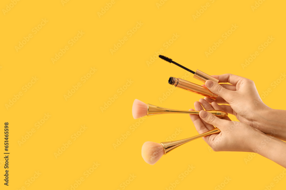 Woman with makeup brushes and mascara on yellow background