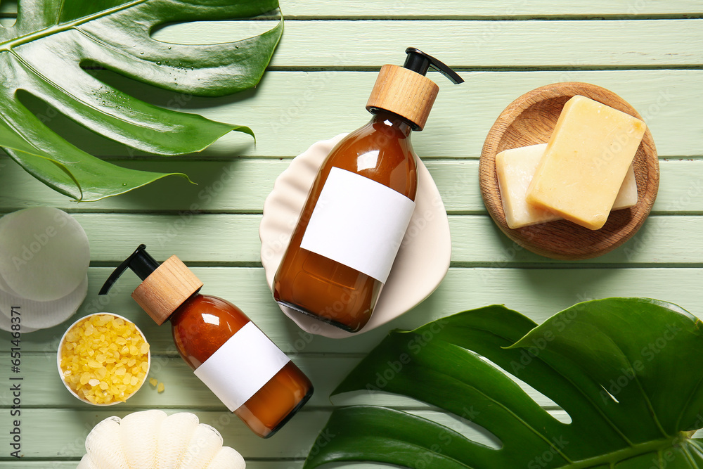 Bottles of shampoo, soap, sea salt and cotton pads on green wooden background