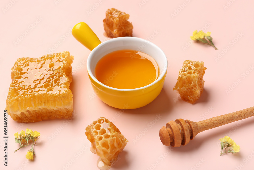 Bowl with tasty honey, honeycomb, dipper and beautiful flowers on pink background, closeup