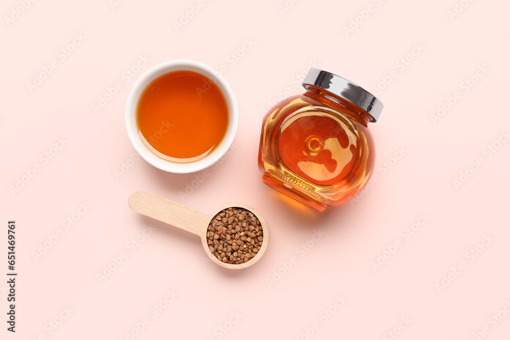 Jar with tasty honey and raw buckwheat on pink background