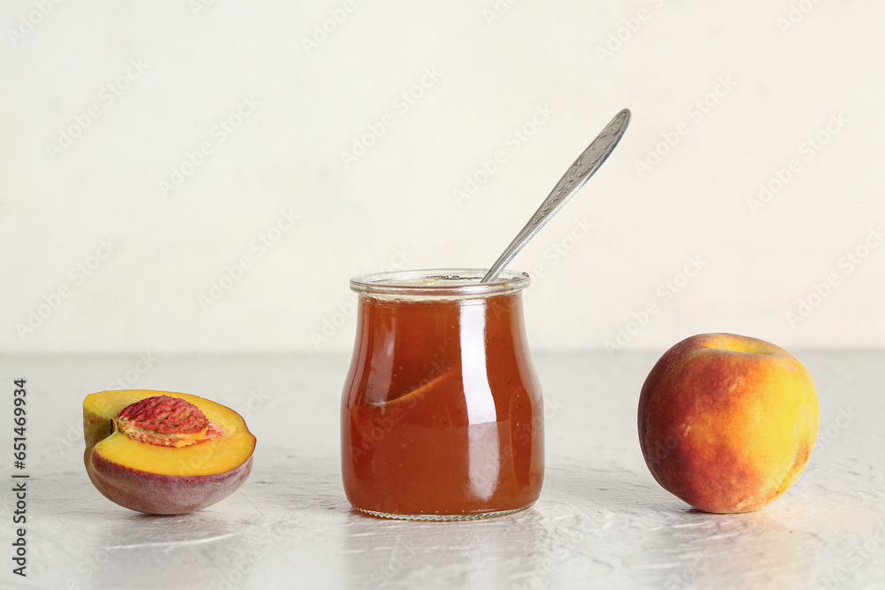 Jar with sweet peach jam and fresh fruits on light background