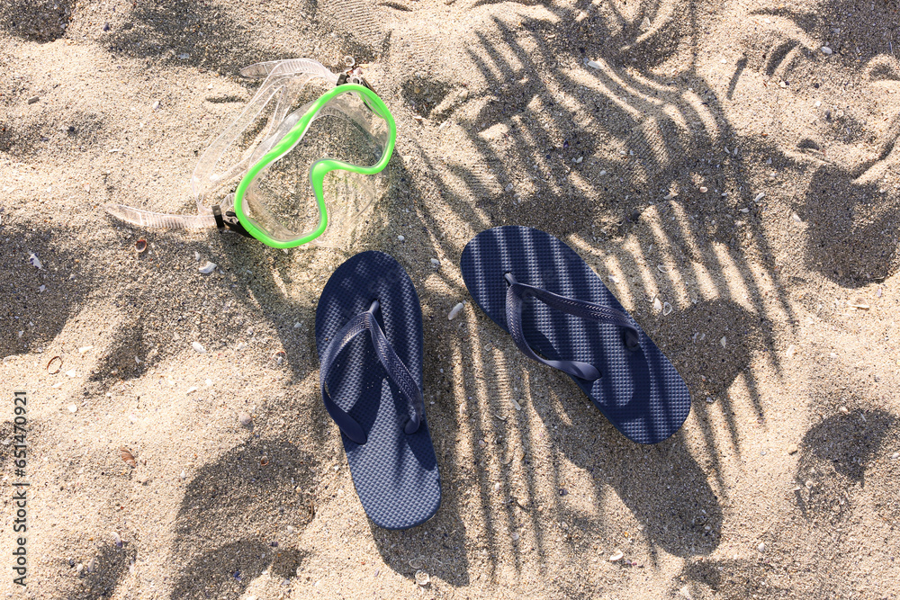 Stylish female blue flip flops and snorkeling mask on sand