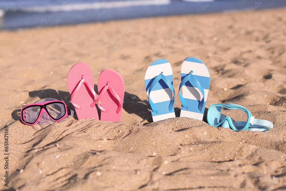 Different stylish female flip flops and snorkeling masks on sand