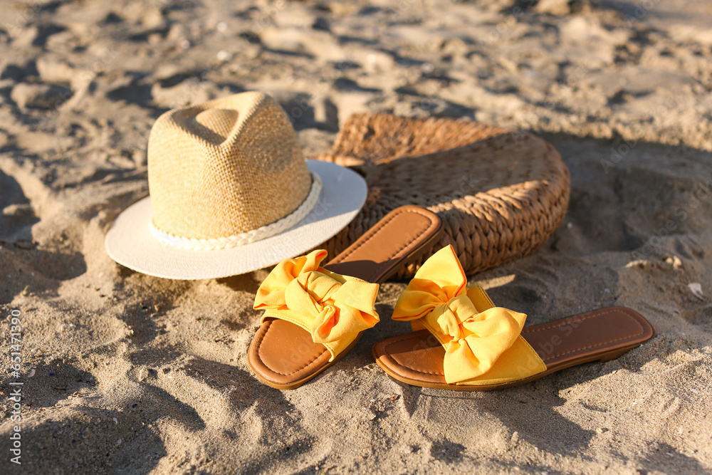 Stylish female flip flops, female hat and bag on sand