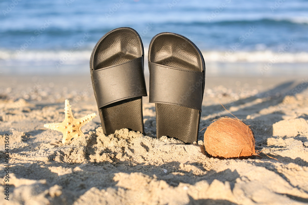 Stylish female flip flops, starfish and coconut on sand