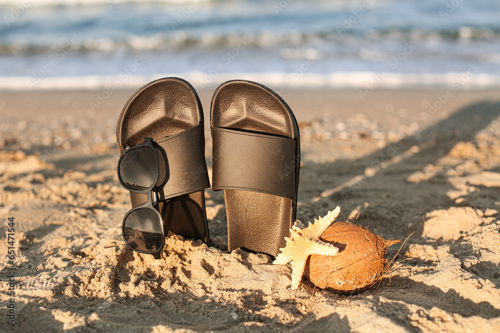 Stylish female flip flops, starfish and coconut on sand