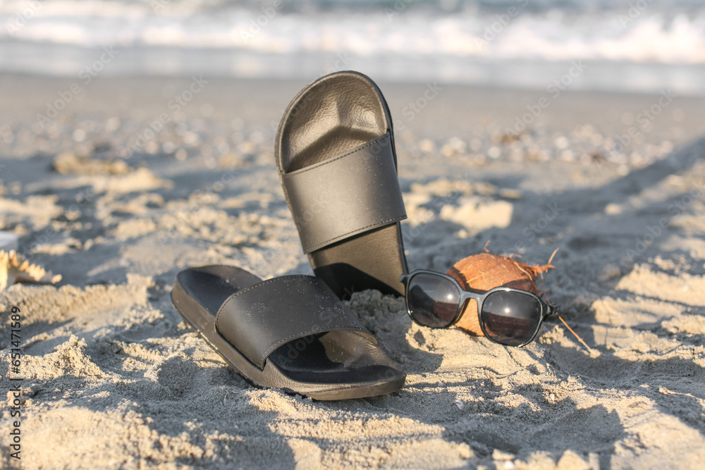 Stylish female flip flops, sunglasses and coconut on sand