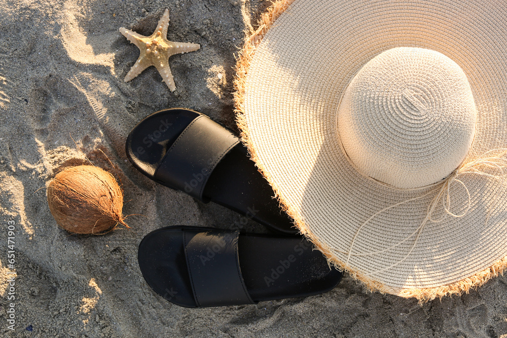 Stylish female flip flops, hat, coconut and starfish on sand