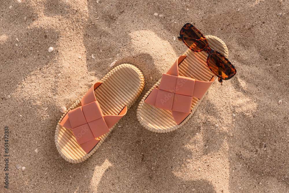 Stylish female flip flops and sunglasses on sand