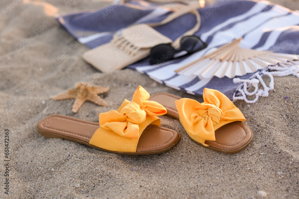 Stylish female flip flops and starfish on sand, closeup