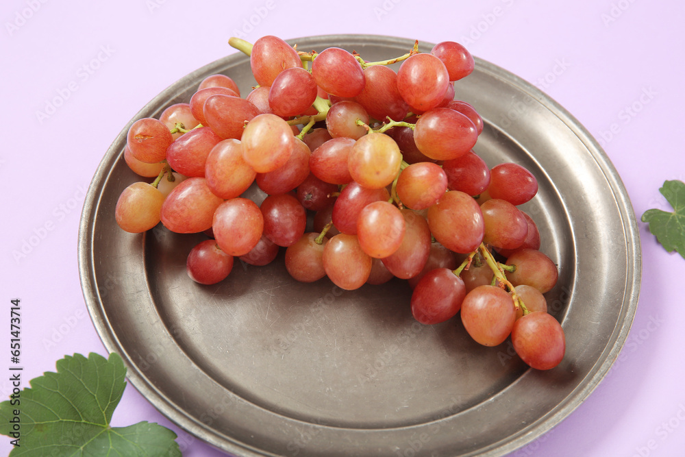 Plate with tasty ripe grapes on lilac background