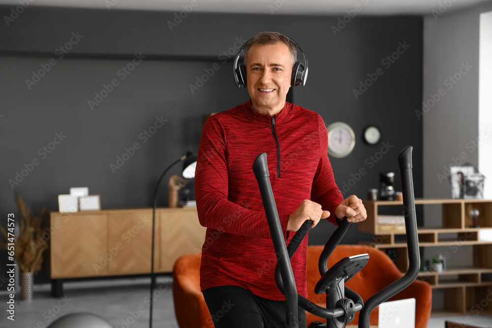 Sporty mature man in headphones training on elliptical at home