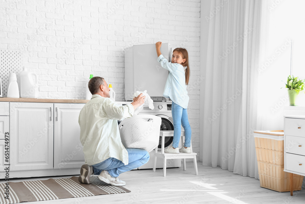 Mature man with his little granddaughter doing laundry at home