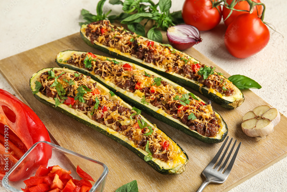 Wooden board with meat stuffed zucchini boats on light background