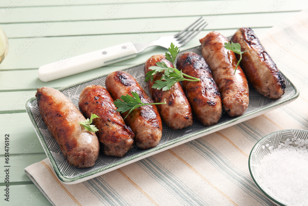 Plate of tasty grilled sausages on green wooden background