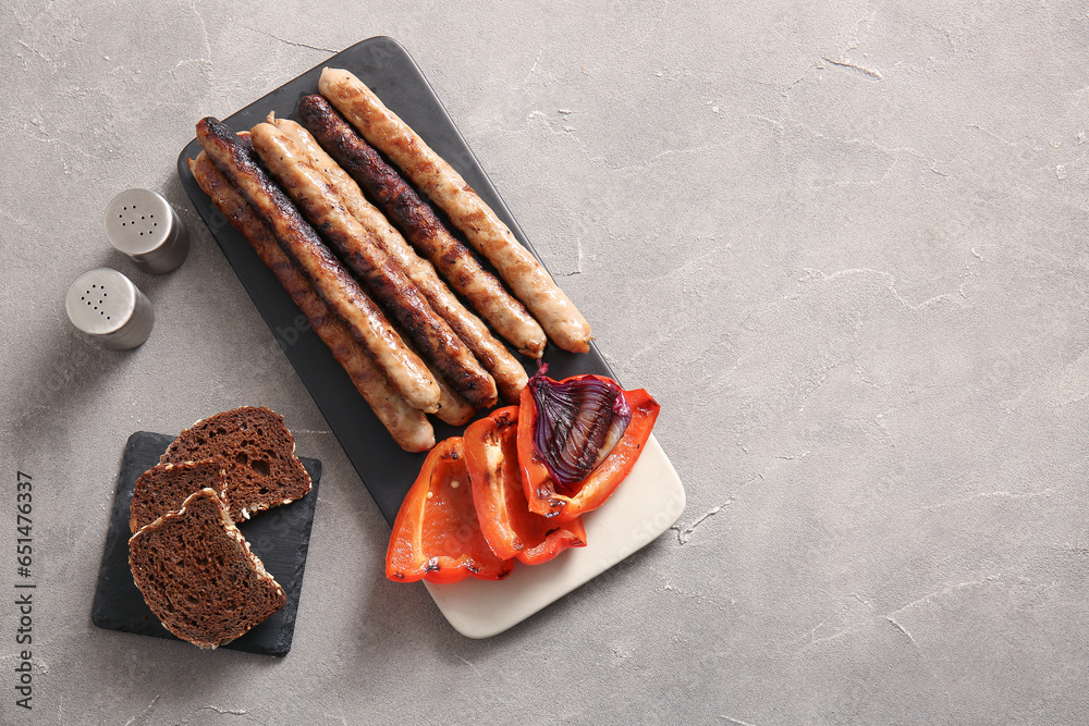 Board of tasty grilled sausages, bread and vegetables on grey background