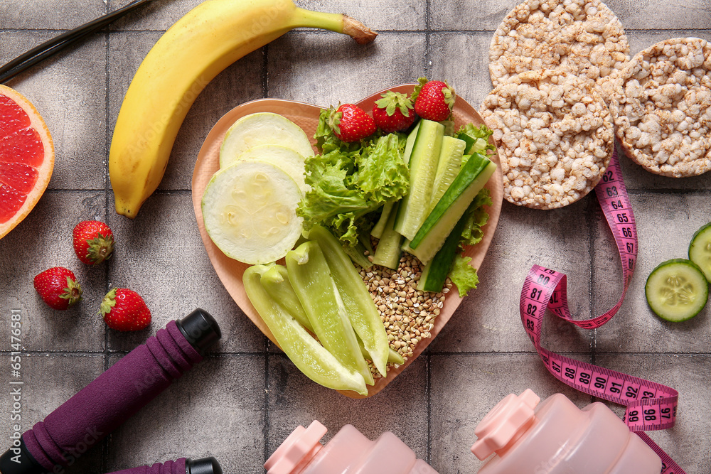 Plate with fresh healthy products and dumbbells on grey tile background. Diet concept