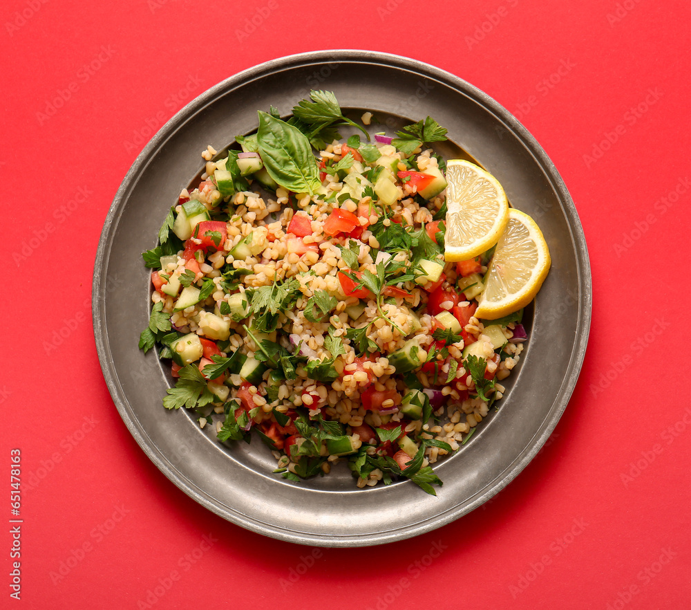 Plate with delicious tabbouleh salad and lemon slices on red background