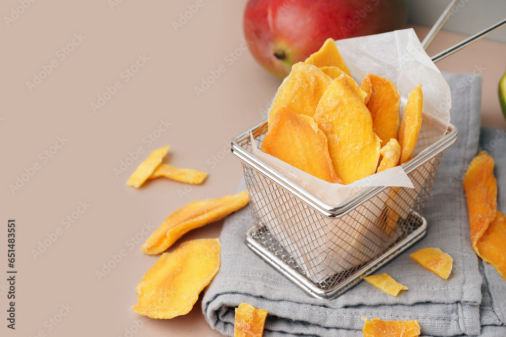 Metal bowl with slices of dried mango on beige background