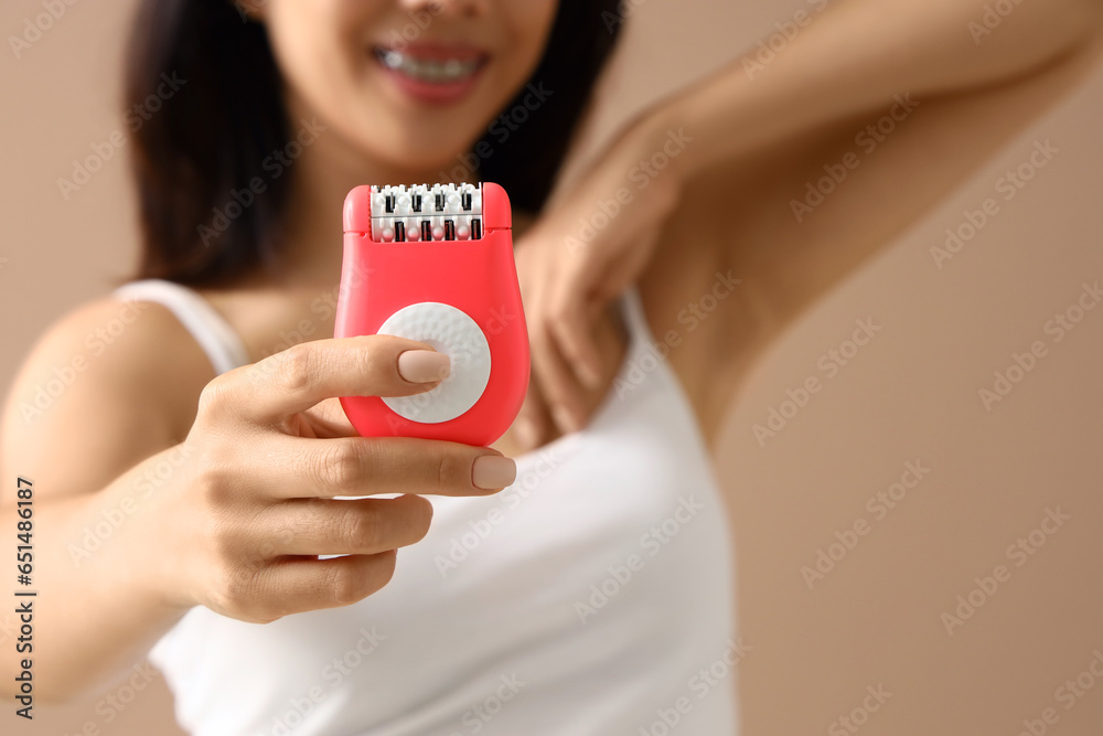 Young woman with epilator on beige background, closeup