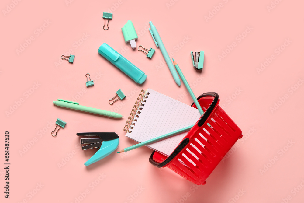 Red shopping basket with different school stationery on pink background