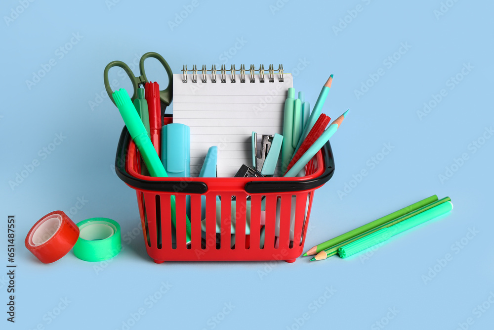 Red shopping basket with different school stationery on blue background