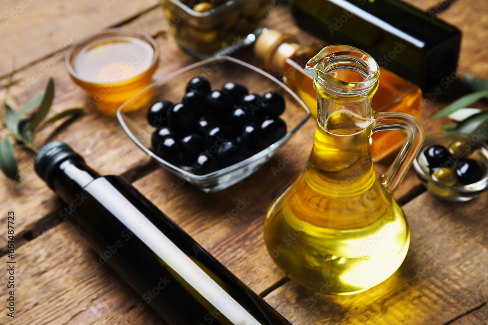 Jug and bottle of fresh olive oil on wooden background