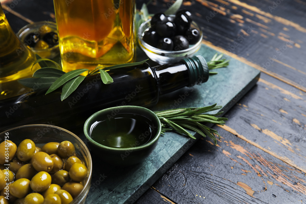 Bowls with olives and oil on black wooden background