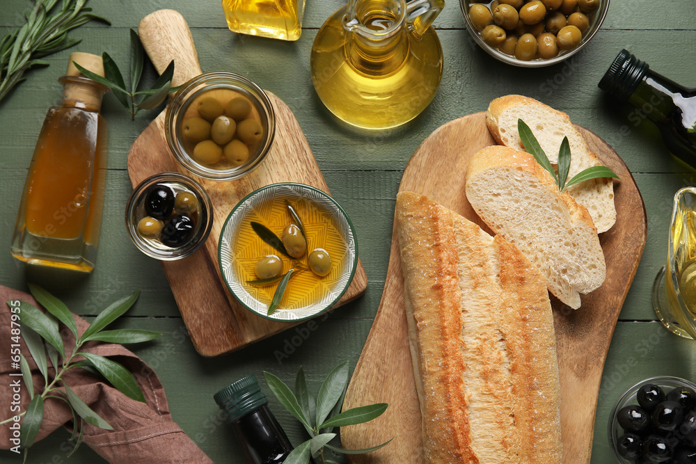 Bowls and different glassware of fresh olive oil with bread on green wooden background