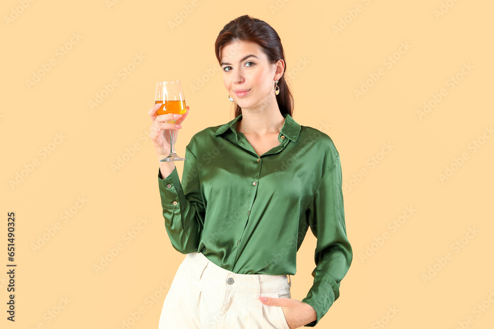 Beautiful young woman with glass of wine on beige background