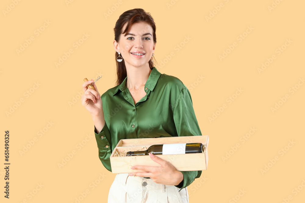 Beautiful young woman with corkscrew and bottle of wine on beige background