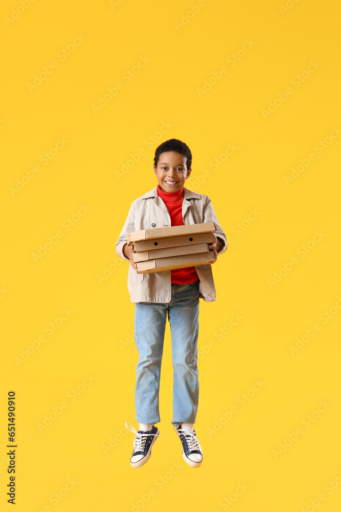 African-American little boy with pizza boxes jumping on yellow background