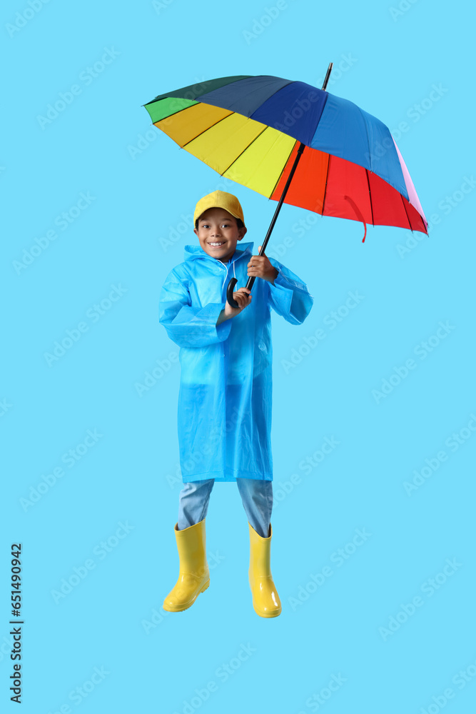 African-American little boy in raincoat with umbrella jumping on blue background