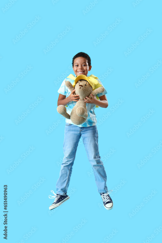 African-American little boy with toy bear jumping on blue background