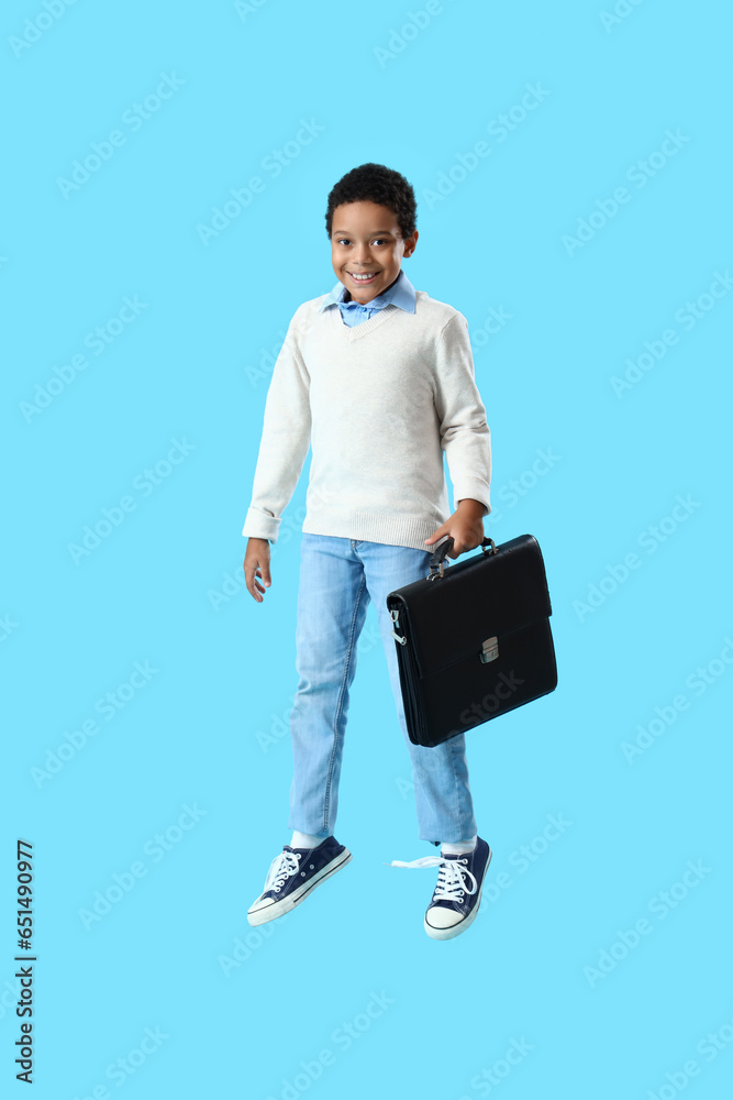 African-American little boy with briefcase jumping on blue background