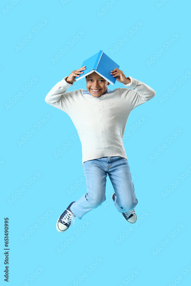 African-American little boy with book jumping on blue background