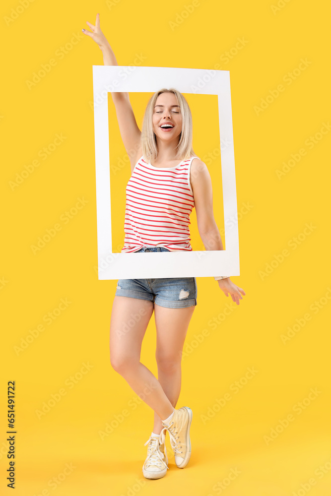 Young beautiful happy woman with frame on yellow background