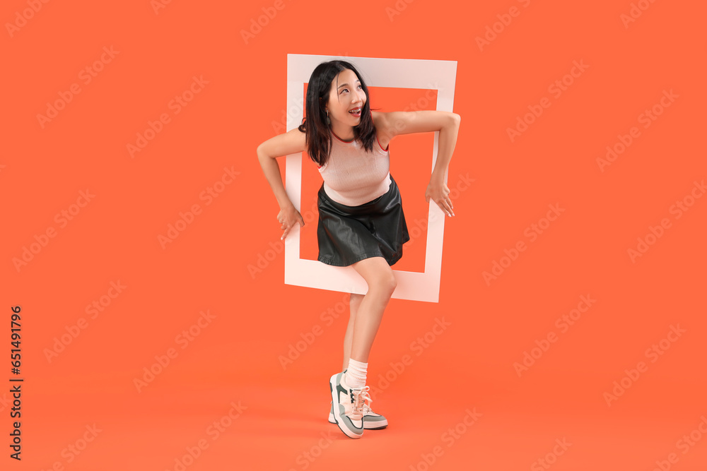 Young beautiful Asian woman with frame on orange background