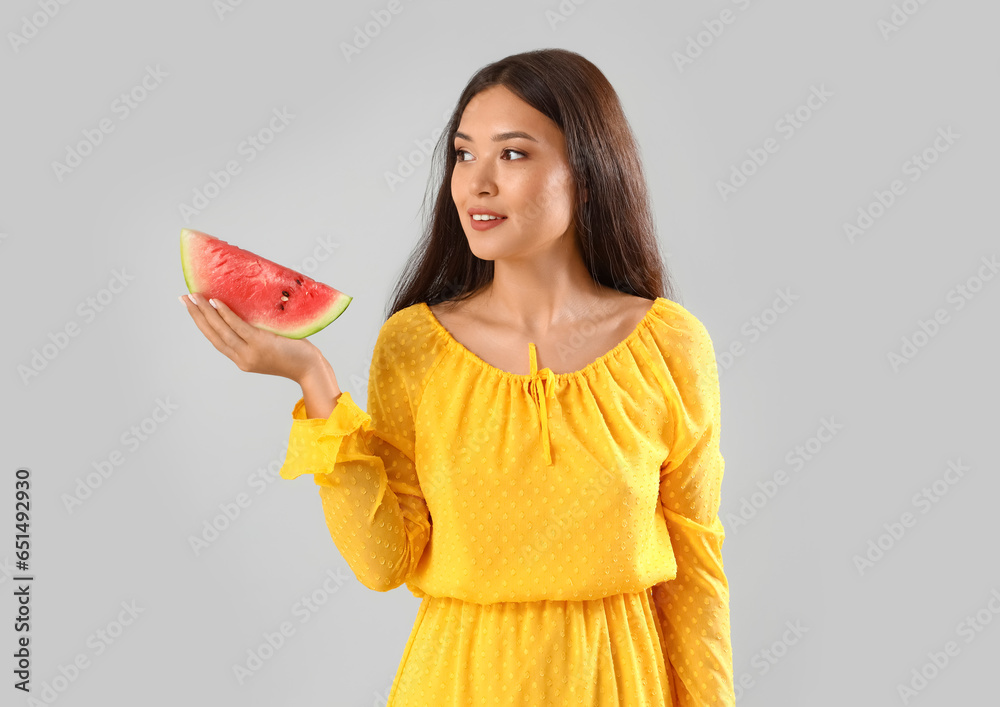 Beautiful young Asian woman with slice of fresh watermelon on grey background