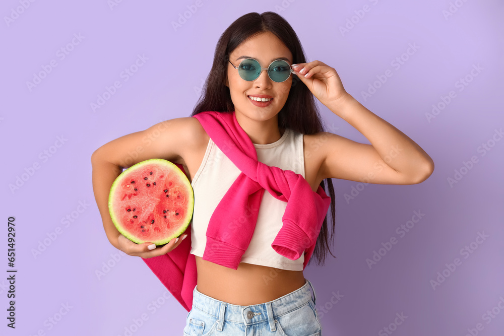 Beautiful young Asian woman with half of fresh watermelon on lilac background