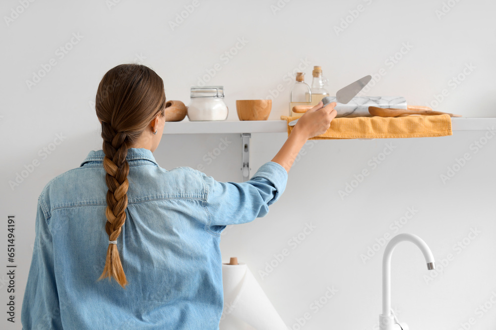 Woman putting spatula on shelf with set of utensils for bakery in kitchen