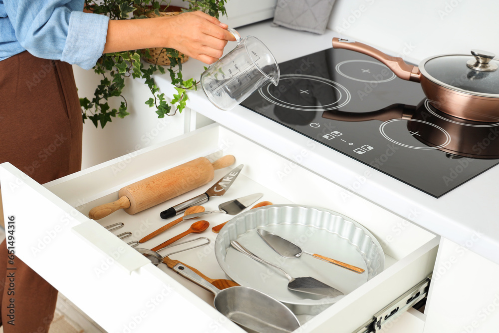 Woman putting measuring cup into kitchen drawer