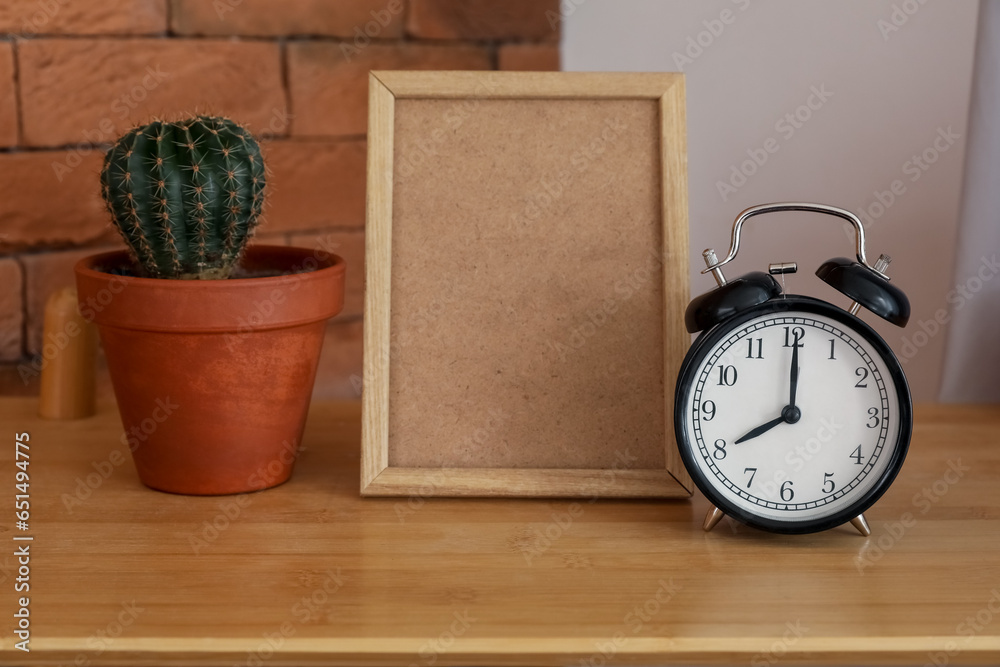 Alarm clock, blank frame and cactus on wooden table, closeup