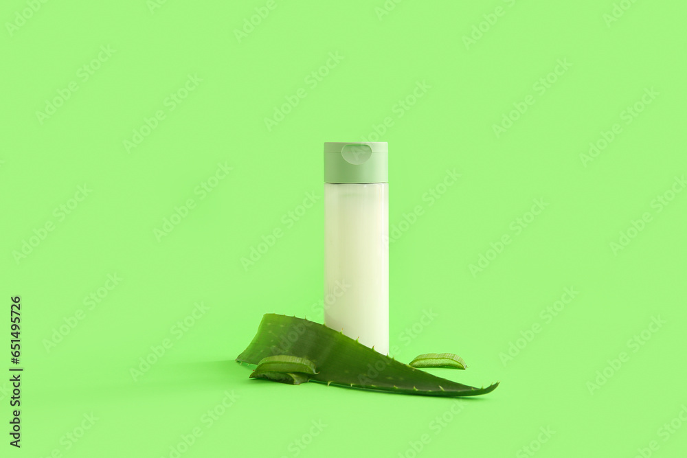 Bottle of cosmetic product and aloe vera leaves on green background