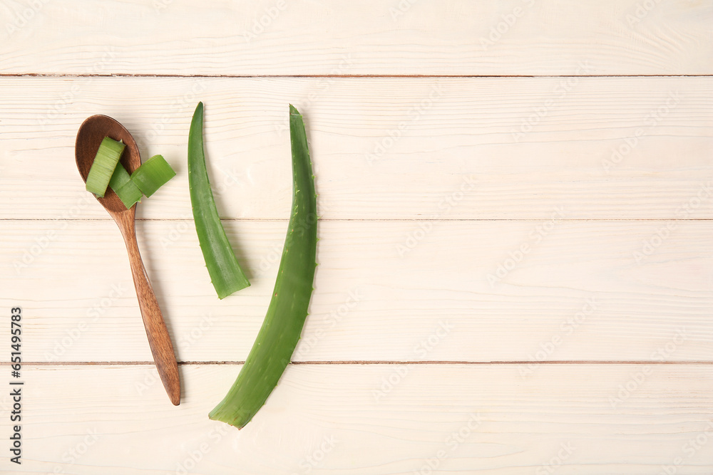 Aloe vera leaves and spoon on white wooden background