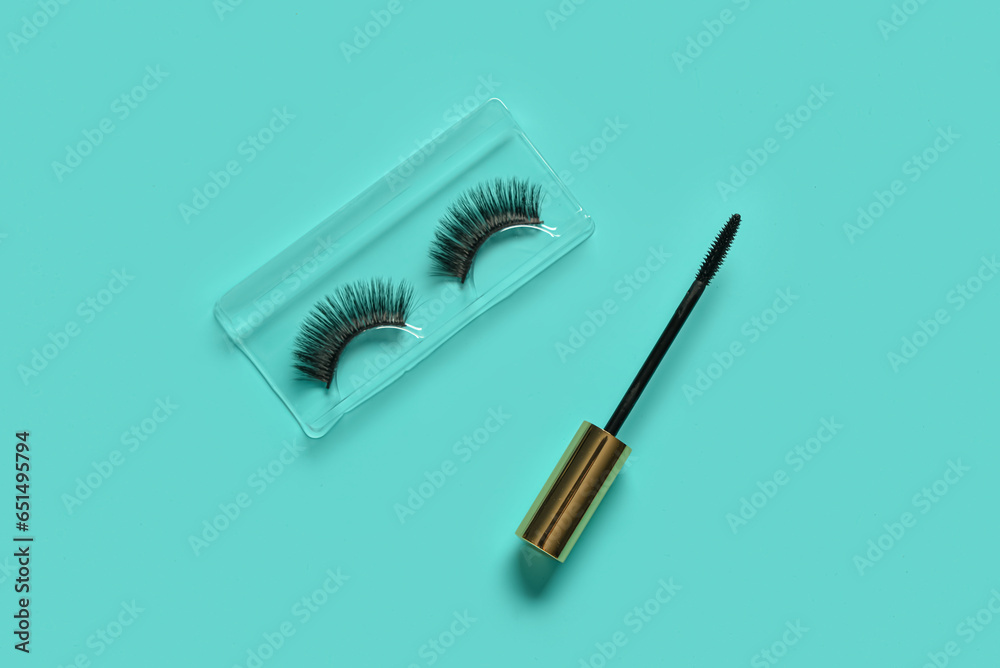 Black mascara brush and fake eyelashes on turquoise background