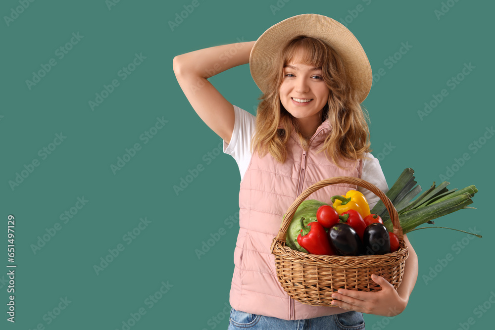 Happy young female farmer with wicker basket full of different ripe vegetables on green background