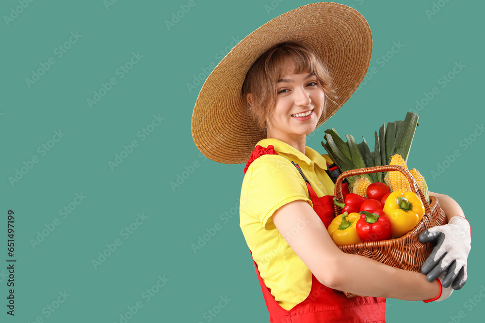 Happy young female farmer with wicker basket full of different ripe vegetables on green background